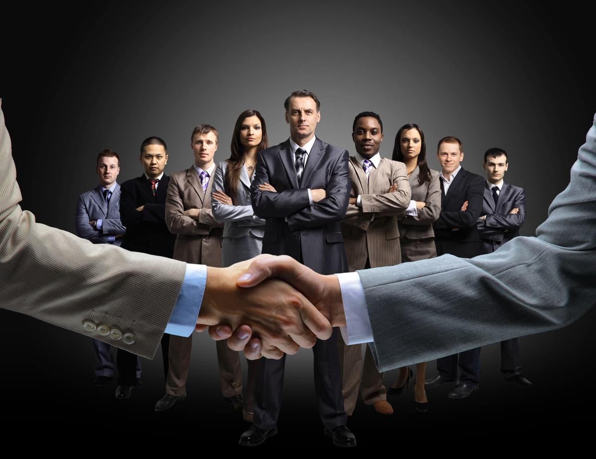 Leaders from government, academia and industry shaking hands in front of a standing team